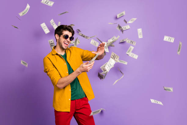 Photo of white cheerful brown haired trendy casual man with bristle, throwing cash with crazy emotions on face in red pants yellow shirt isolated violet pastel color background